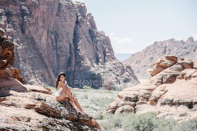 Young woman in white swimsuit sitting on rocks on canyon with cliffs and peaks. — Stock Photo