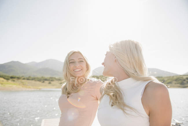 Zwei blonde Teenager-Mädchen sitzen auf einem sonnigen Steg und schauen einander an. — Stockfoto