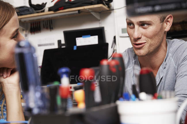 Jovem mulher e homem conversando no laboratório de tecnologia com ferramentas na mesa . — Fotografia de Stock
