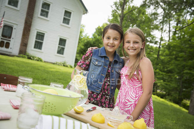 Chicas pre-adolescentes reuniéndose en la mesa del jardín y haciendo limonada fresca . - foto de stock