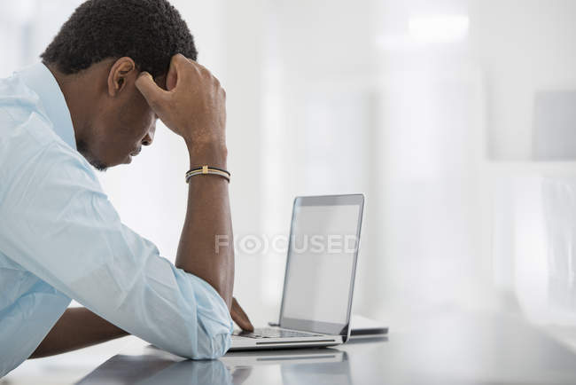 Side view of pensive young man sitting at table and using laptop. — Stock Photo