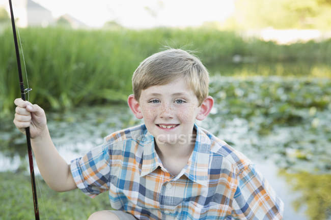 Niño de edad elemental sosteniendo caña de pescar por país río . - foto de stock