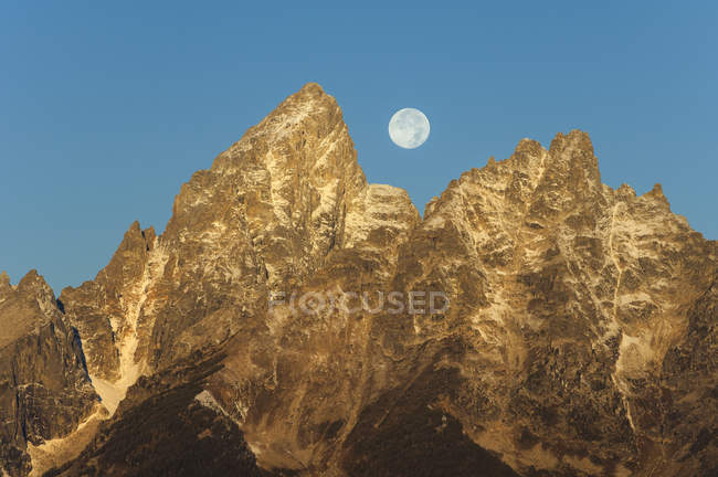 Chaîne de montagnes dentelée dans le parc national du Grand Teton avec pleine lune dans le ciel . — Photo de stock