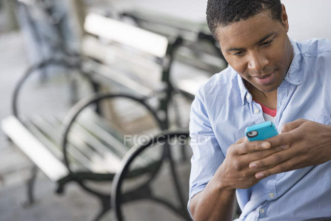 Uomo seduto sulla panchina in città e utilizzando smartphone . — Foto stock