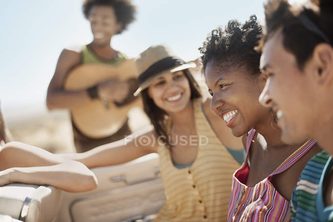 Group of friends in convertible having fun with guitar. — Stock Photo