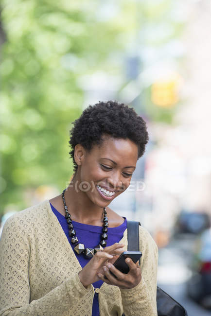 Жінка середнього віку з коротким волоссям перевіряє смартфон на вулиці . — стокове фото