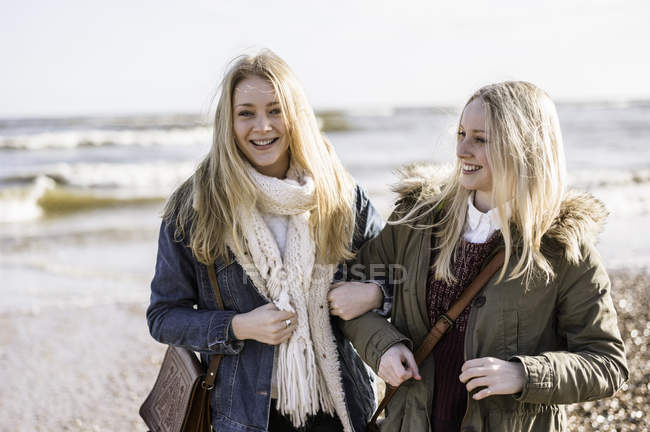 Two young women standing arm in arm on beach in winter. — Stock Photo