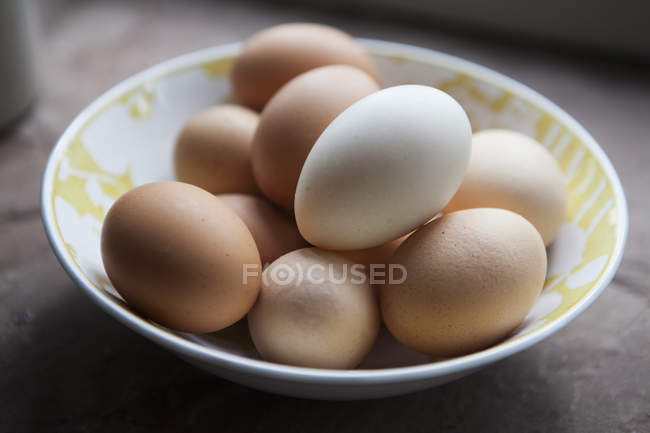 Schüssel mit Eiern mit hellen und braunen Schalen auf dem Tisch. — Stockfoto
