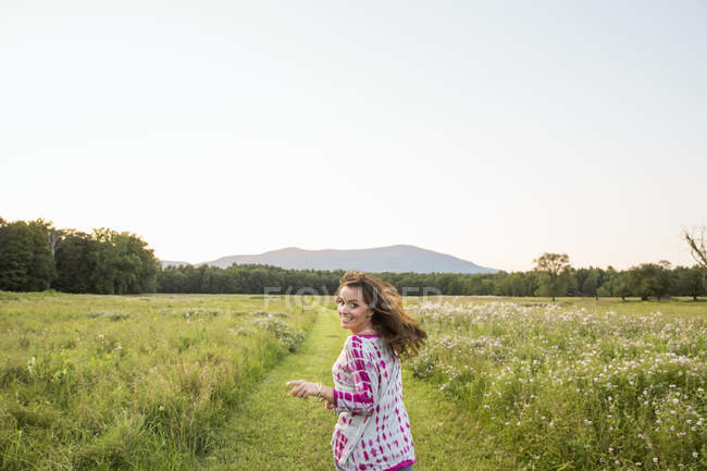 Mulher correndo ao longo do caminho no prado e olhando sobre o ombro . — Fotografia de Stock