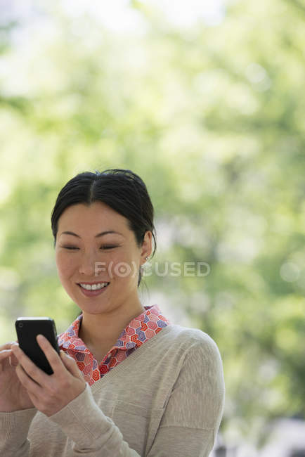 Asiatin checkt Smartphone im Stadtpark. — Stockfoto