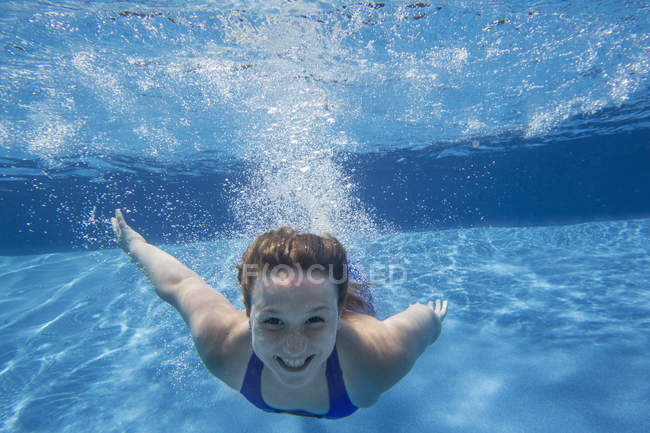 Cheerful pre-adolescent girl swimming underwater in pool. — Stock Photo