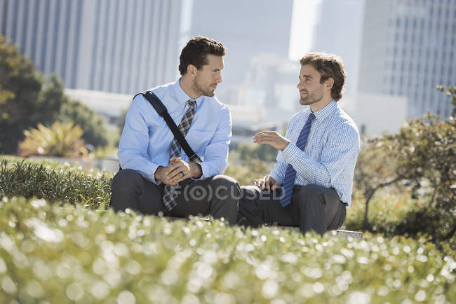 Dois homens de camisas e gravatas sentados e conversando no parque da cidade
. — Fotografia de Stock