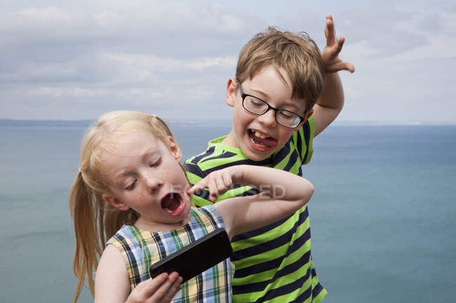 Brother and sister making faces and taking selfie with smartphone. — Stock Photo