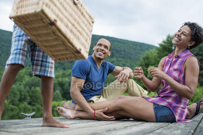 Сім'я сидить на пірсі з хлопчиком початкового віку з кошиком для пікніка . — стокове фото