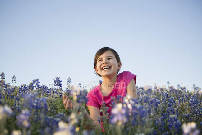 Pre-adolescent girl sitting in field of wild flowers and laughing. — Stock Photo