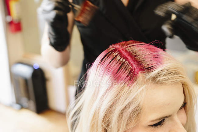 Жіночого волосся колорист в рукавички, застосовуючи руде волосся фарби для клієнта світле волосся з пензлем. — стокове фото