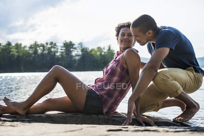Casal sentado juntos no cais por lago no verão . — Fotografia de Stock