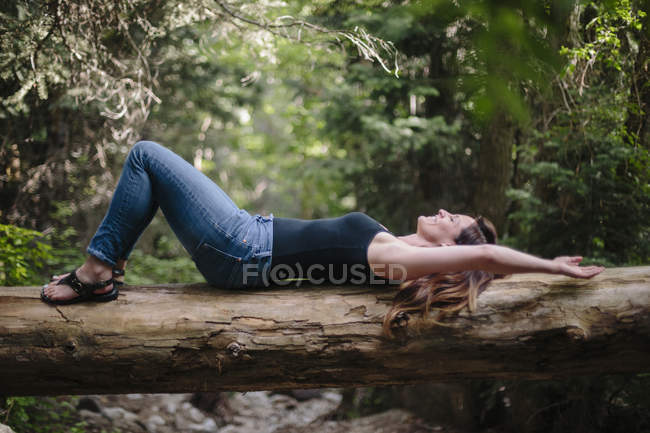 Frau liegt auf Rücken auf umgestürztem Baumstamm im Wald. — Stockfoto