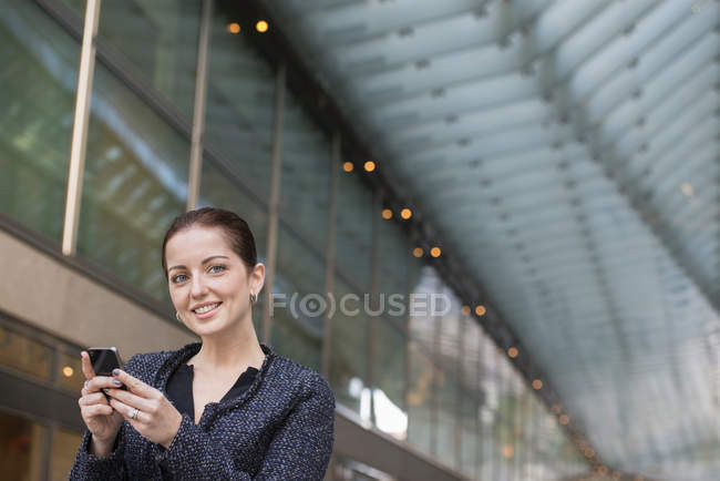 Mitte erwachsene Geschäftsfrau in grauer Jacke nutzt Smartphone und schaut weg. — Stockfoto