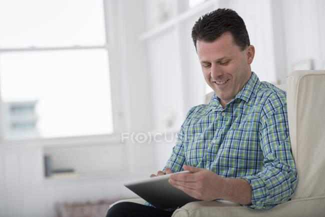 Homem maduro sentado em poltrona e usando tablet digital
. — Fotografia de Stock