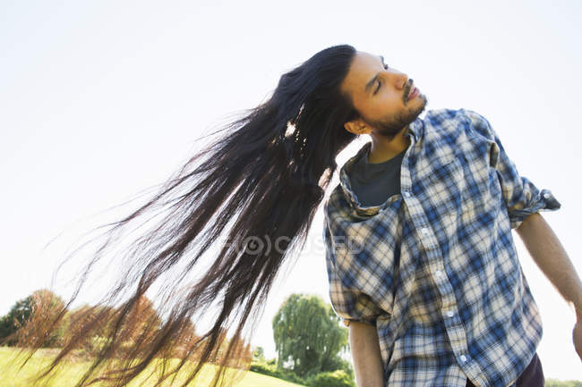 Молодий чоловік з довгим темним волоссям трясе голову і пірнає на свіжому повітрі . — стокове фото