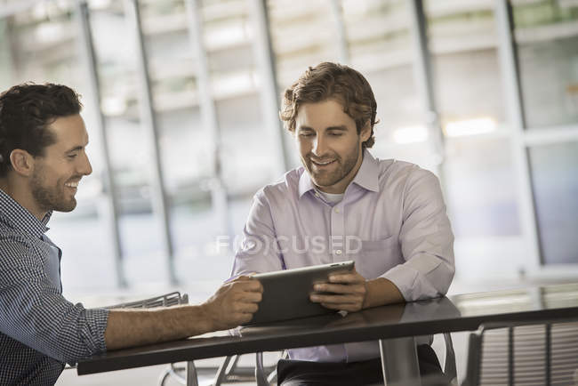 Two men looking at digital tablet while sitting at table in street cafe. — Stock Photo