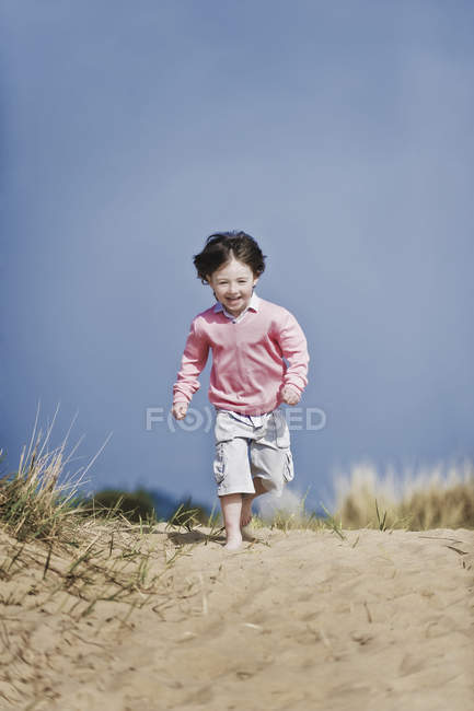 Мальчик младшего возраста с каштановыми волосами бегает по пляжу . — стоковое фото