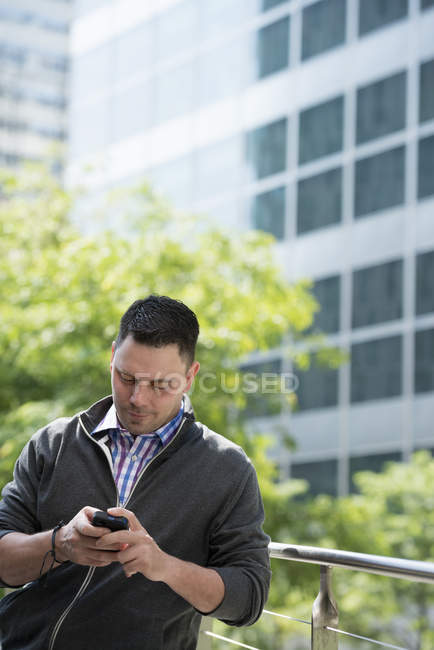 Uomo medio adulto appoggiato su ringhiera nel parco e controllo smartphone . — Foto stock