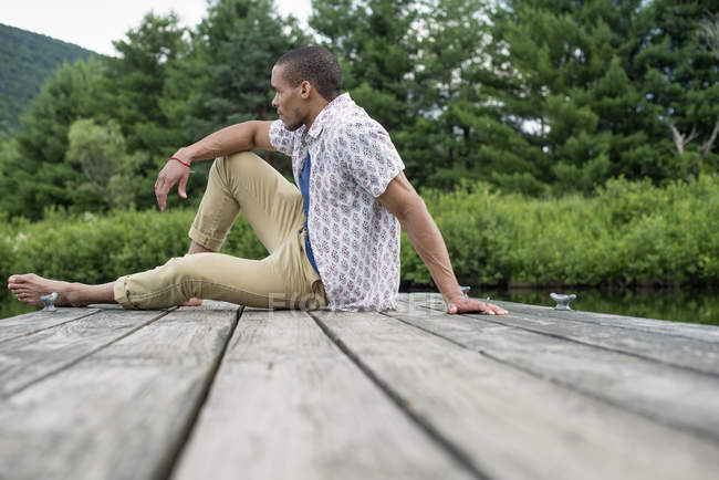 Mitte erwachsener Mann sitzt im Sommer auf Holzsteg am See — Stockfoto