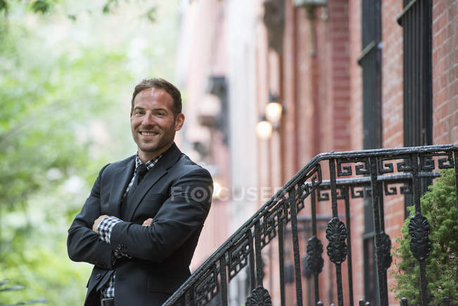 Homme en costume debout sur les marches du bâtiment en grès brun avec les bras croisés . — Photo de stock