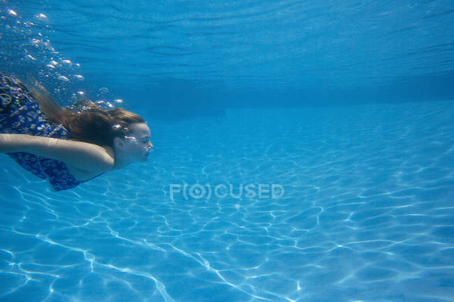 Pré-adolescente avec ventilateur cheveux longs nageant sous l'eau dans la piscine . — Photo de stock
