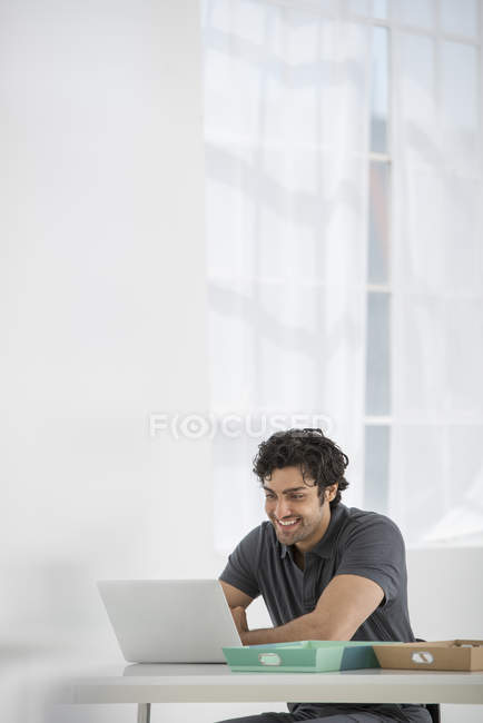 Jovem sentado na mesa e usando laptop no escritório . — Fotografia de Stock