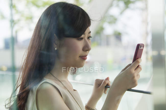 Mulher usando smartphone no prédio de escritórios atrás do painel de vidro . — Fotografia de Stock