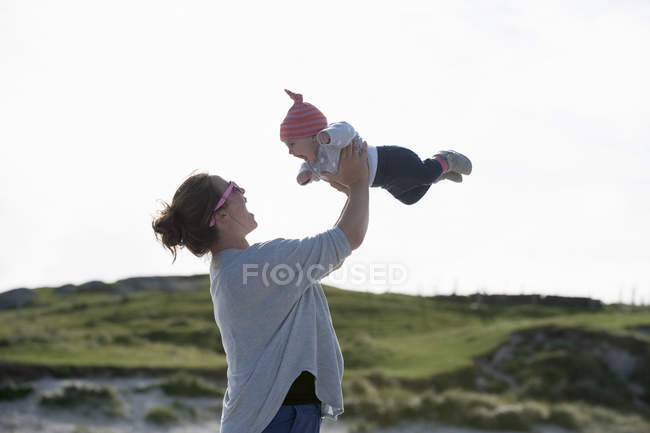 Madre criando al bebé en el aire en la playa . - foto de stock