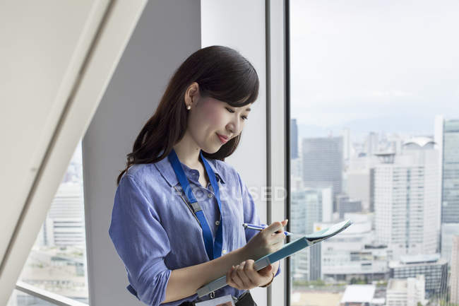 Giovane donna d'affari in possesso di file e guardando giù in edificio per uffici . — Foto stock