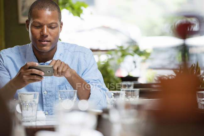 Man sitting in city cafe by table with glasses and crockery and checking phone. — Stock Photo