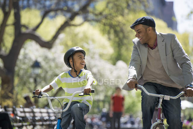 Father and son cycling on bicycles side by side in sunny park. — Stock Photo