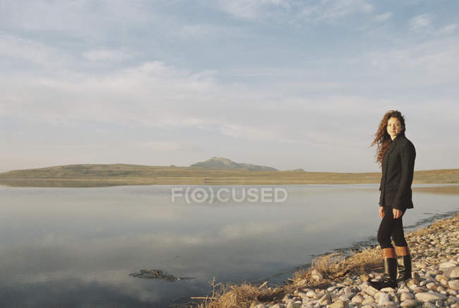 Mid adult woman standing on rocky shore of lake. — Stock Photo