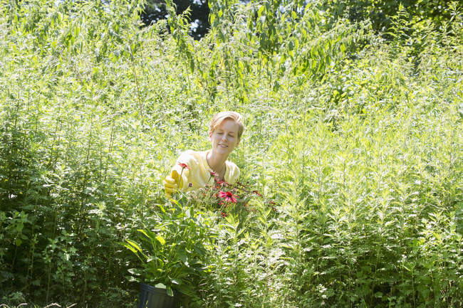 Mulher entre flores e grama verde alta no viveiro de plantas . — Fotografia de Stock