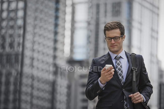 Businessman in suit and tie checking smartphone on city street. — Stock Photo
