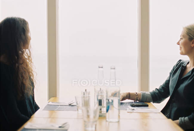 Две женщины сидят за столом и смотрят в большое окно . — стоковое фото