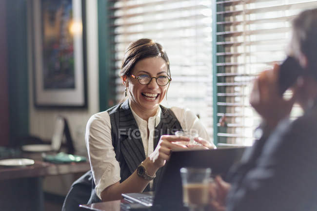 Mujer riendo y sosteniendo la taza de café en el escritorio de la oficina con el hombre hablando por teléfono en primer plano . - foto de stock