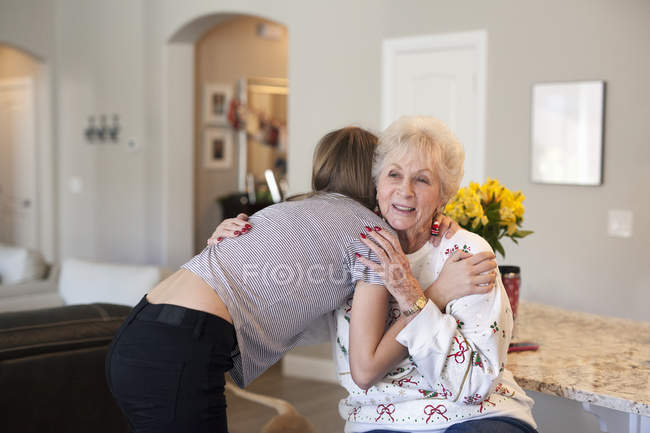 Adolescente menina abraçando mulher sênior em casa interior . — Fotografia de Stock