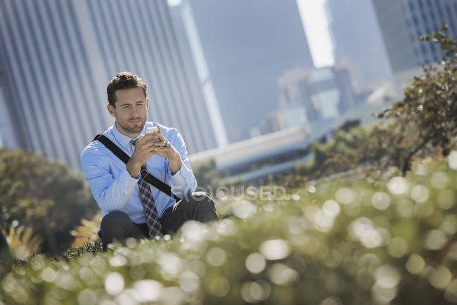 Junger Mann sitzt auf Parkbank in der Stadt und benutzt Smartphone. — Stockfoto
