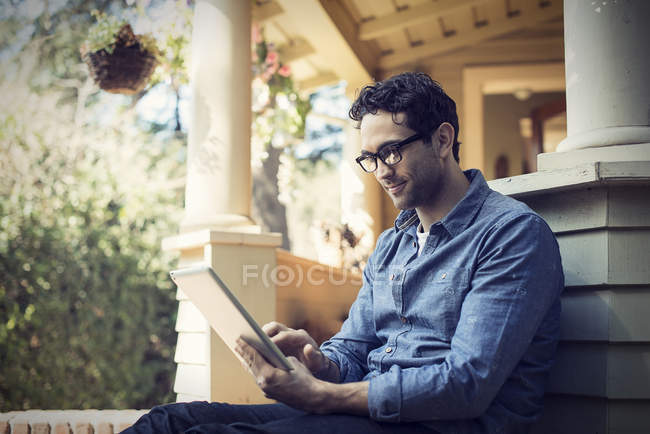 Hombre usando tableta digital en el porche en la casa de campo . - foto de stock