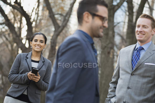Businessmen and businesswoman with smartphone relaxing in city park. — Stock Photo