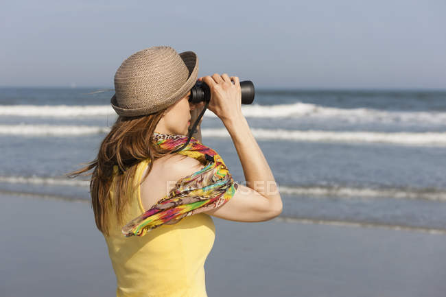 Donna in cappello da sole e sciarpa con binocolo sulla spiaggia del New Jersey Shore, USA . — Foto stock