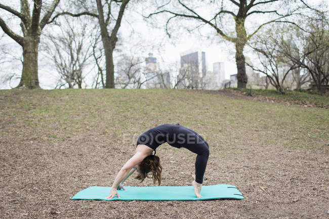 Frau wölbt sich im Central Park auf Yogamatte zurück. — Stockfoto