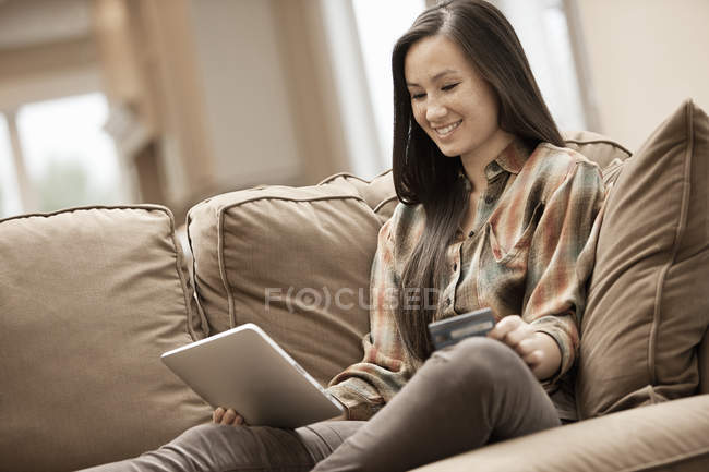 Donna seduta su divano e shopping online con tablet digitale e carta di credito . — Foto stock