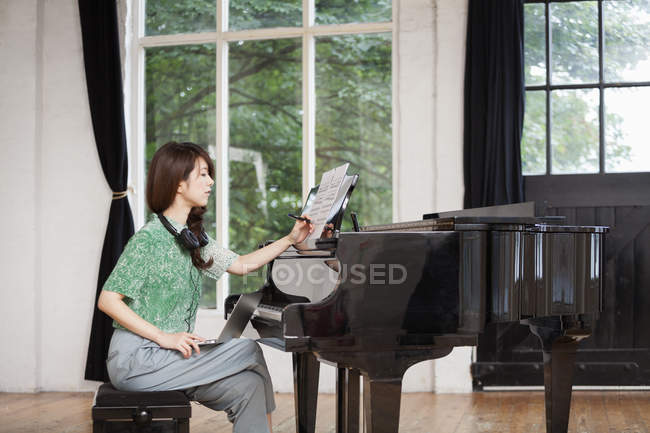 Giovane donna seduta al pianoforte a coda in studio di prova e annotare spartiti . — Foto stock
